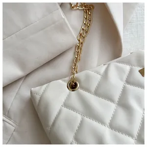 Detail of white quilted tote bag with golden chain strap and metallic ring accents