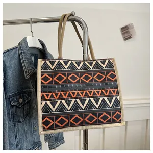 Detail of bohemian tote bag with geometric tribal print and woven handles near denim jacket