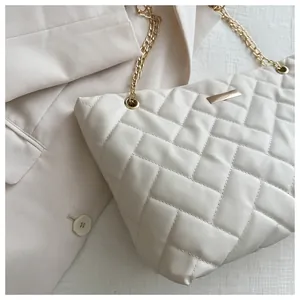 Detailed macro view of the cream quilted texture and gold chain on the luxury tote bag