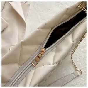 Close-up of beige quilted tote bag showing smooth metal zipper and gold chain strap