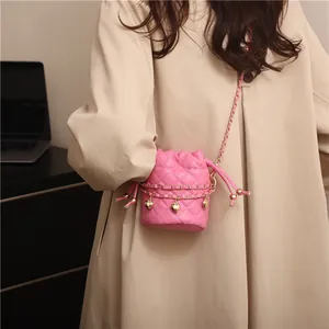 Rosa gesteppte Mini-Eimertasche mit Goldkette und Herzanhänger am Model in beigem Mantel