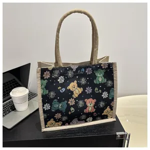 Gros plan du sac cabas noir en toile avec ours colorés posé sur un bureau avec café