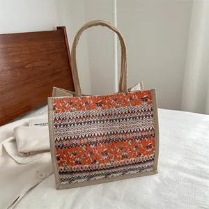 Bohemian jute tote bag with orange floral print and woven handles on a bed