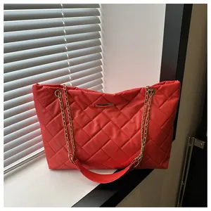 Detail of red quilted tote bag with gold chain strap and metallic logo plate