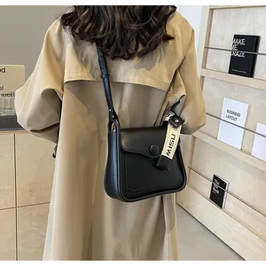Detailed view of a black leather square crossbody bag worn with a khaki trench coat