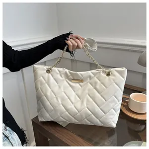 Close-up of white quilted tote bag featuring gold chain strap and elegant metal clasp detail