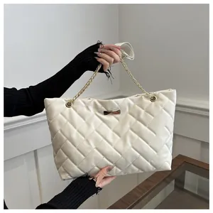 Detail of cream quilted tote bag featuring a gold metal plaque and chain leather strap