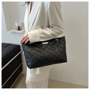 Detail of black quilted tote bag with V-shaped texture and gold chain shoulder strap