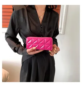 Détail d'une pochette en cuir verni matelassé rose tenue par un mannequin en tenue noire