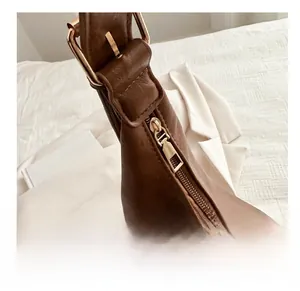 Detailed close-up of smooth golden zipper and metal buckle on brown leather tote bag