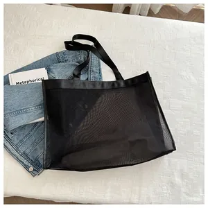 Detalle de un bolso shopper de malla negra con asas reforzadas sobre un fondo con estilo