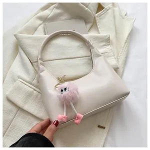 Dettaglio di una borsa hobo a mezzaluna bianco crema con ciondolo mostro di peluche