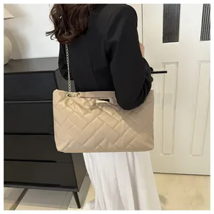 Close-up of beige quilted tote bag with gold chain strap and metal logo on a model