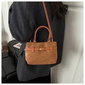 Sac seau en daim marron avec boucle dorée porté sur un manteau en laine gris chic