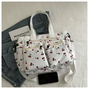 Detailed flat lay of white cherry print tote bag with multiple zip pockets and wide strap
