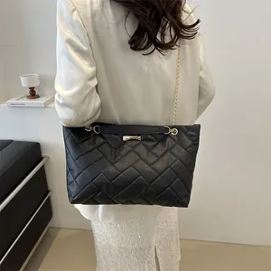 Large black quilted leather tote bag with gold chain strap carried by fashion model