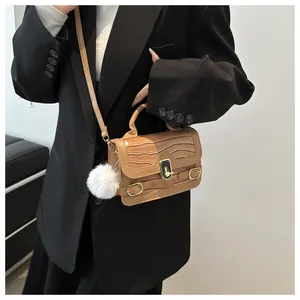 Detail der khakifarbenen Mini-Umhängetasche mit Kroko-Prägung, Goldschnalle und Plüschball