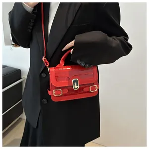 Detail der roten Krokostruktur-Handtasche mit goldener Schließe auf schwarzem Blazer