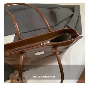 Primer plano del bolso tote marrón brillante con cremallera y detalle metálico plateado