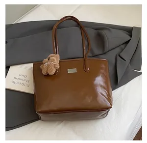 Detalle de bolso tote de cuero marrón brillante con colgante de oso y placa plateada