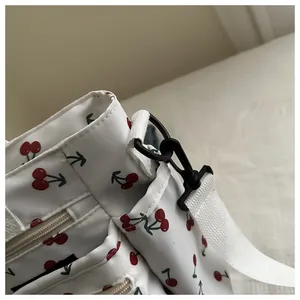Close-up of cherry print crossbody bag showing zipper, white strap, and black hardware