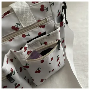 Detail view of large white canvas shoulder bag with cherry print and side storage pockets