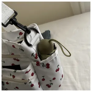 Close-up of white canvas tote with cherry print, external pockets and a mini green umbrella