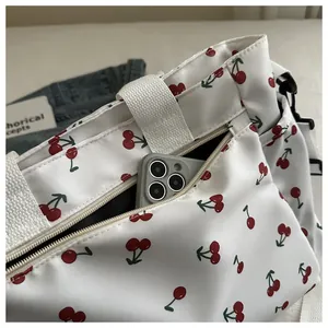 Close-up of white cherry print crossbody bag with zipper pocket and phone for size scale
