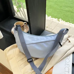 Detail of light blue nylon crescent bag on a neutral fabric with lifestyle accessories