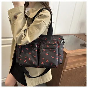 Detail of a black nylon tote bag featuring red cherry prints and multiple utility pockets