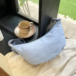 Close-up of a light blue nylon crescent bag with adjustable strap in a bright window setting