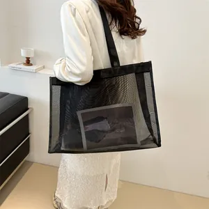 Bolso tote grande de malla negra con bolsillo interior llevado por modelo para playa