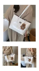 Detalle del bolso tote de charol blanco brillante con un bonito colgante de oso marrón