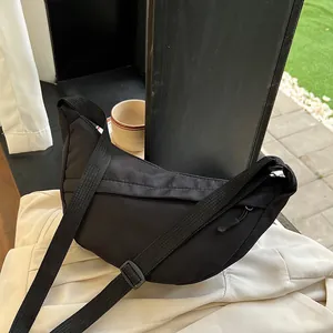 Minimalist black nylon crescent crossbody bag with adjustable strap on fabric background