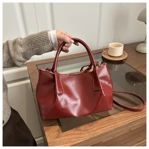 Detail of wine red crossbody bag with glossy texture and handles in lifestyle setting