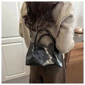 Close-up of black glossy pleated handbag with round handles and long shoulder strap