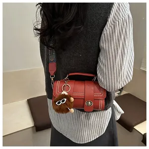 Détail du petit sac rouge avec rivets brillants et bandoulière large à motifs ethniques