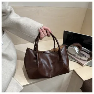 Detail of glossy dark brown pleated handbag with top handle in professional office setting