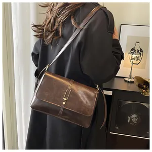 Detail of vintage brown leather crossbody bag with metal rivet closure on black coat