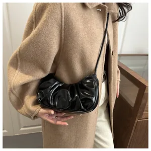 Vue latérale du sac croissant noir brillant plissé porté avec un manteau en laine
