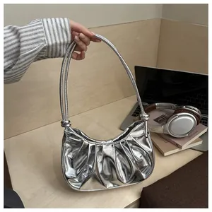 Détail du sac à bandoulière argenté plissé avec poignée nouée dans un décor quotidien