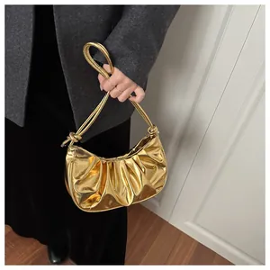 Détail du sac à bandoulière doré plissé avec poignée nouée porté par un modèle