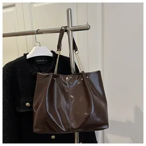 Detail view of large dark brown patent leather tote bag with gold chain strap