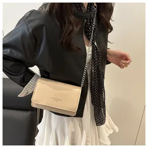 Detail van een beige lakleren crossbody tas met kettingriem en elegante typografie
