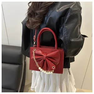 Vue latérale d'un sac à main rouge avec grand nœud et chaîne en perles sur un modèle