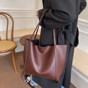 Side view of a dark brown large tote bag in matte faux leather on a model's shoulder