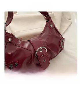 Détails macro du sac en cuir brillant bordeaux avec rivets argentés et boucle métallique