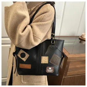 Detailed view of black PU tote bag with vintage patches on khaki wool coat
