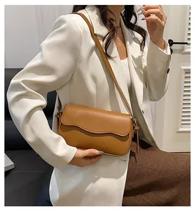 Sac bandoulière en cuir marron avec rabat festonné porté par un mannequin dans un salon