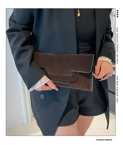 Detail of dark brown envelope clutch bag featuring geometric layered flap and matte texture